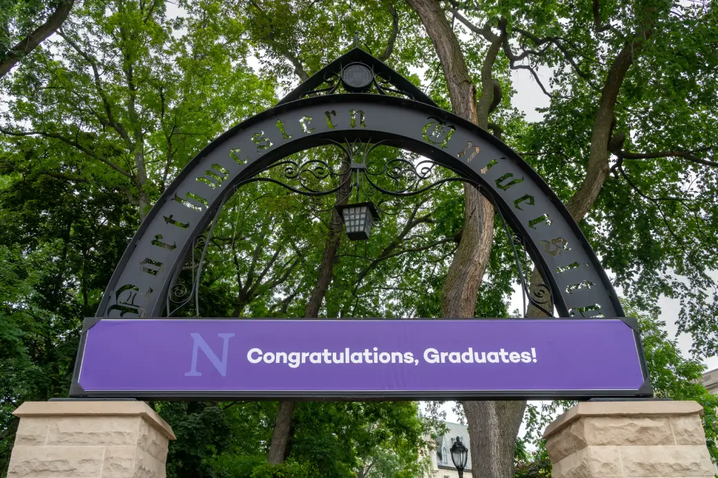Northwestern University arch with a purple banner reading “Congratulations, Graduates!” beneath leafy trees.