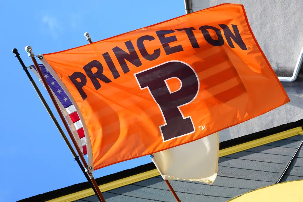 An orange Princeton University flag flying next to American and white flags on Ivy Day
